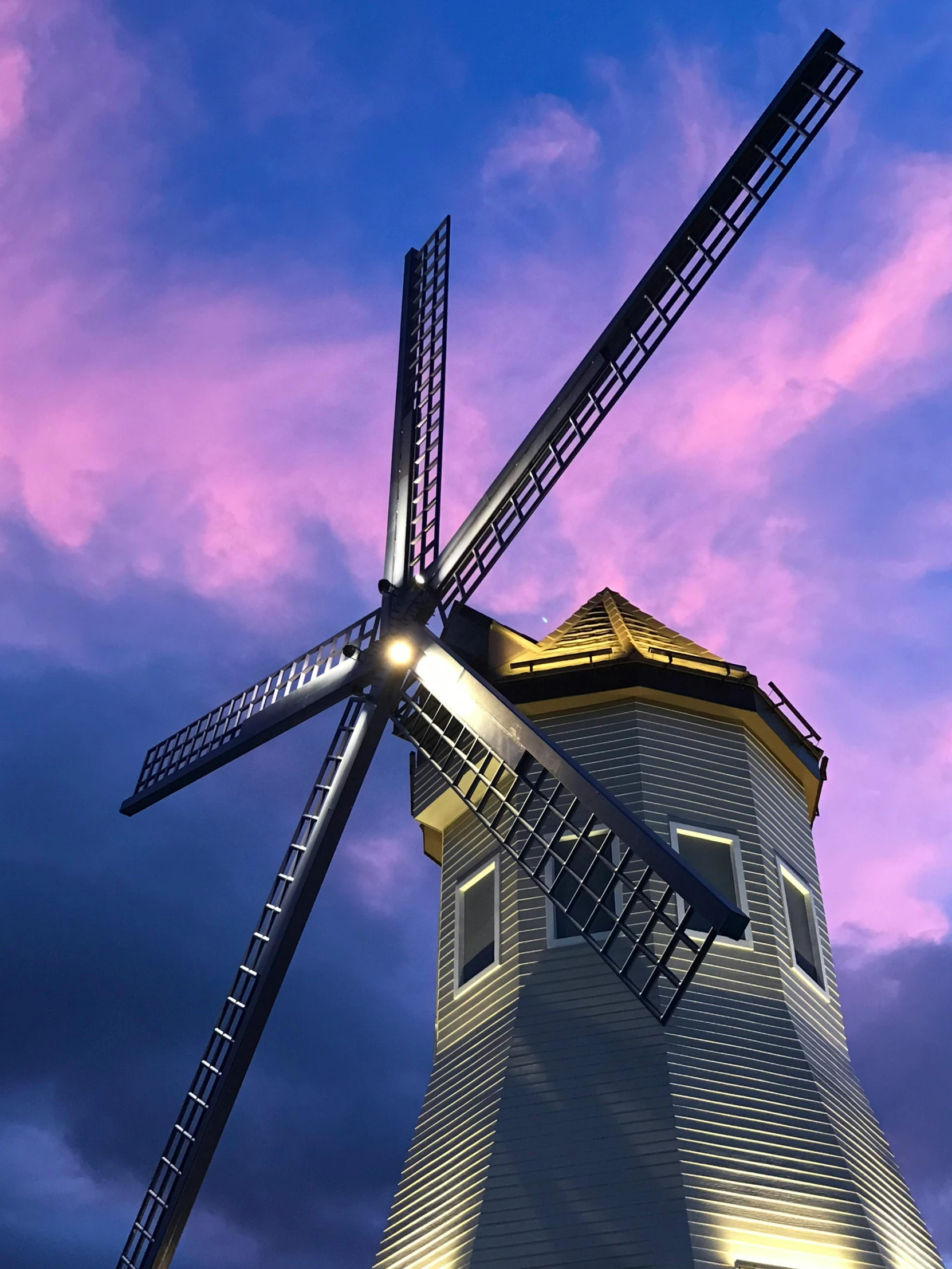 a windmill sitting on top of a lush green field, an album cover, inspired by Phil Koch, pexels contest winner, photorealism, purple and yellow lighting, profile image, taken on iphone 14 pro, pink