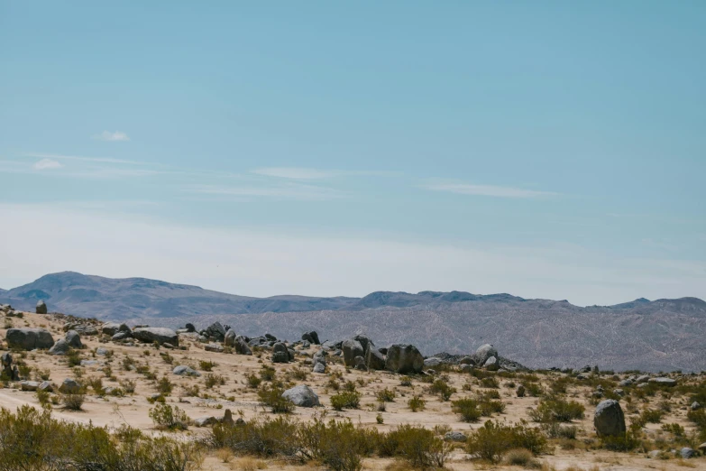 a dirt road in the middle of a desert with mountains in the background, unsplash, visual art, tall big rocks, background image, seen from a distance, hillside desert pavilion