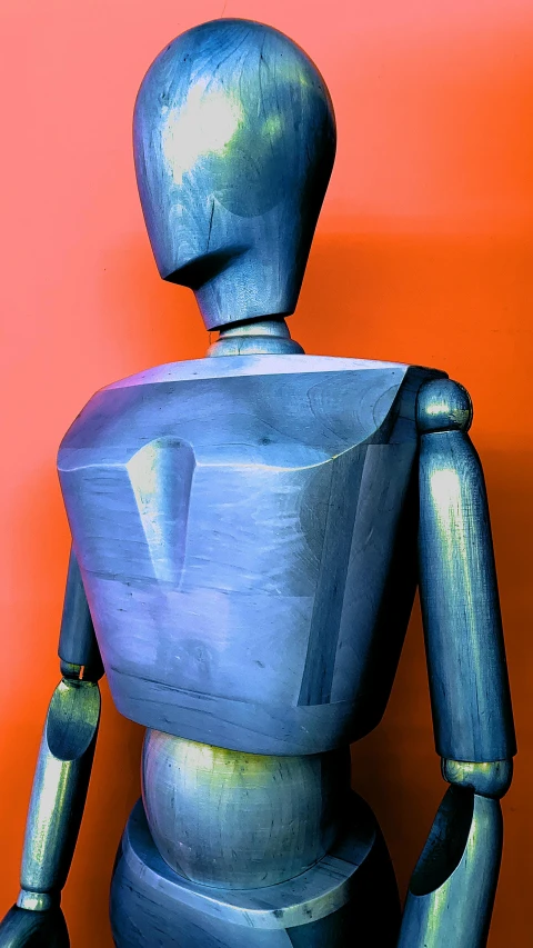 a blue robot standing in front of a red wall, inspired by Oskar Schlemmer, computer art, wooden armor, upper body close - up, 1 9 9 7, ((robot))