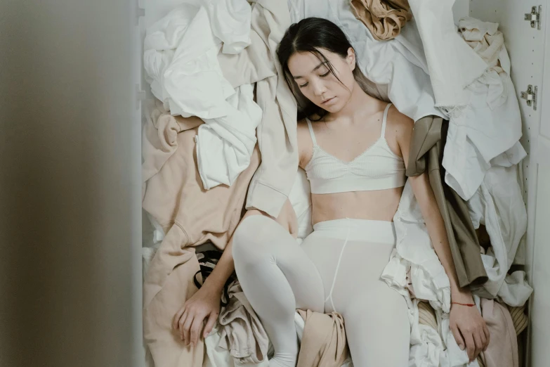 a woman laying on top of a pile of clothes, inspired by Elsa Bleda, pexels contest winner, renaissance, white leggings, young asian girl, beige, tired appearance