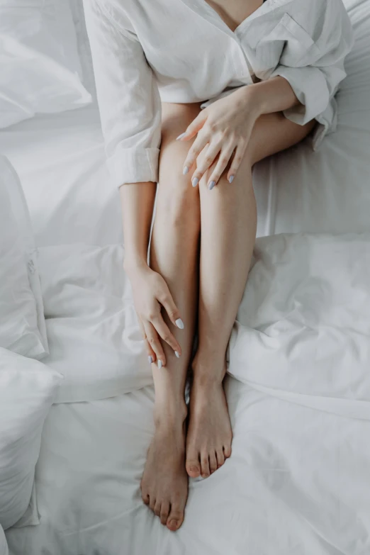 a woman sitting on a bed with her legs crossed, trending on pexels, graceful arms, skin texture natural, detailed white, pearlescent skin