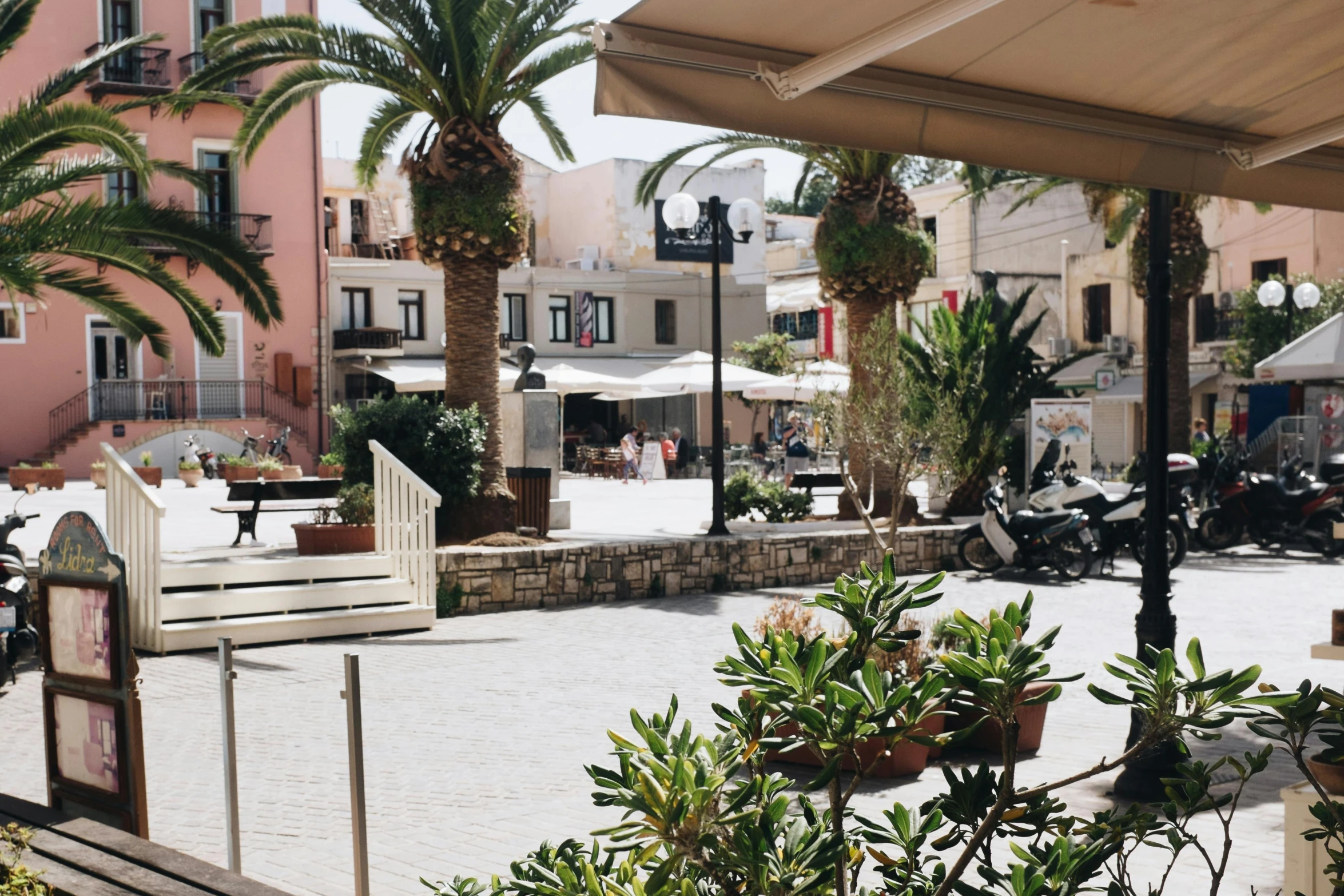 a group of motor scooters parked in front of a building, unsplash, les nabis, mediterranean island scenery, square, plants and patio, people walking around