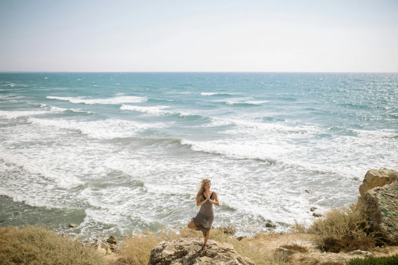 a woman standing on top of a cliff next to the ocean, unsplash, happening, israel, yoga, three views, long distance photo