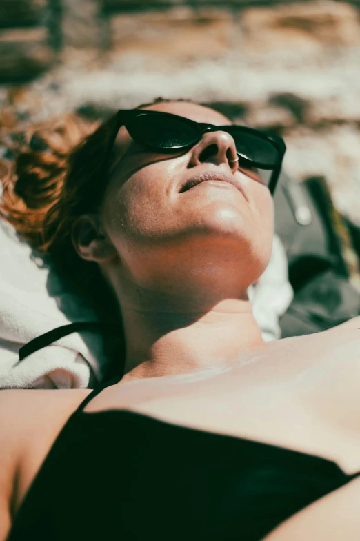 a woman laying on top of a sandy beach, trending on unsplash, figuration libre, in sun glasses, portrait of a woman sleeping, looking upwards, grainy movie still