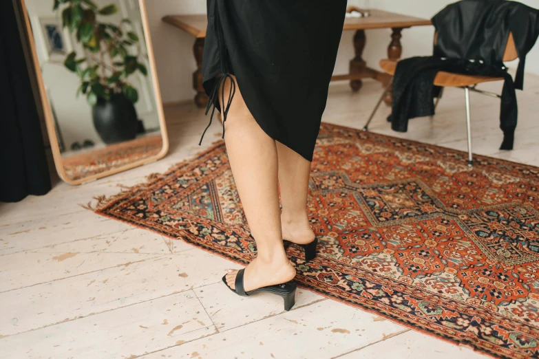 a woman standing on a rug in front of a mirror, unsplash contest winner, wearing black open toe heels, long tails, black and terracotta, she is wearing a black dress