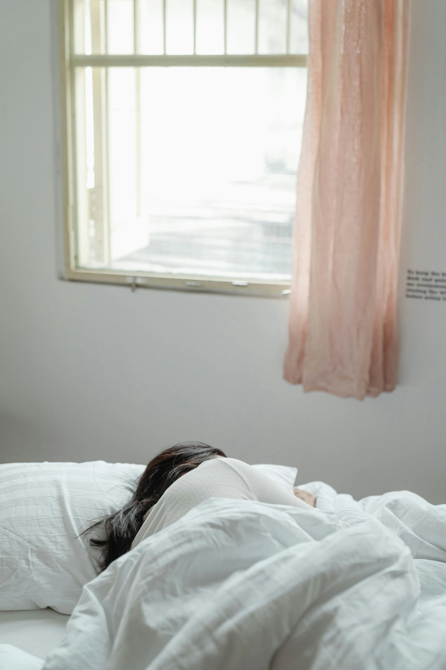 a woman laying on top of a bed next to a window, inspired by Elsa Bleda, unsplash, happening, face down, asian female, hospital, white room