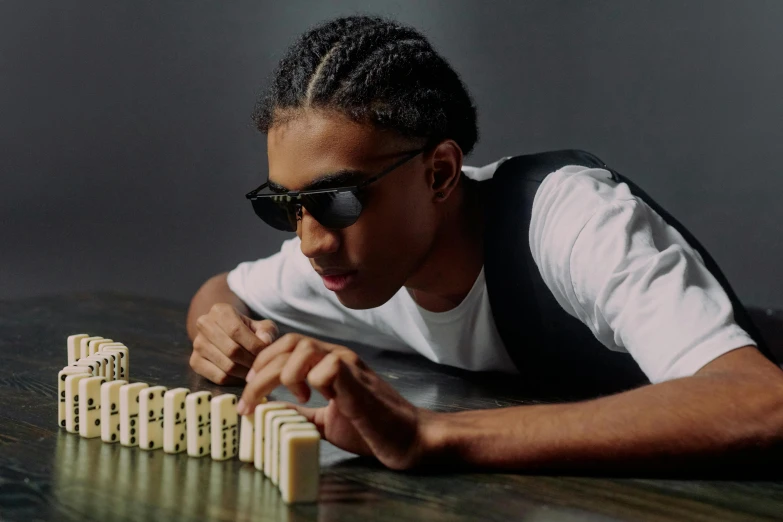 a man sitting at a table with dominos in front of him, an album cover, inspired by David Brewster, trending on pexels, digital sunglasses, black teenage boy, doing an elegant pose, ashteroth