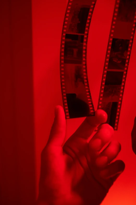 a person holding a film strip in their hand, inspired by Nan Goldin, pexels contest winner, video art, volumetric lighting. red, 2 5 mm portra, 1 9 4 0 s film noir, red wall