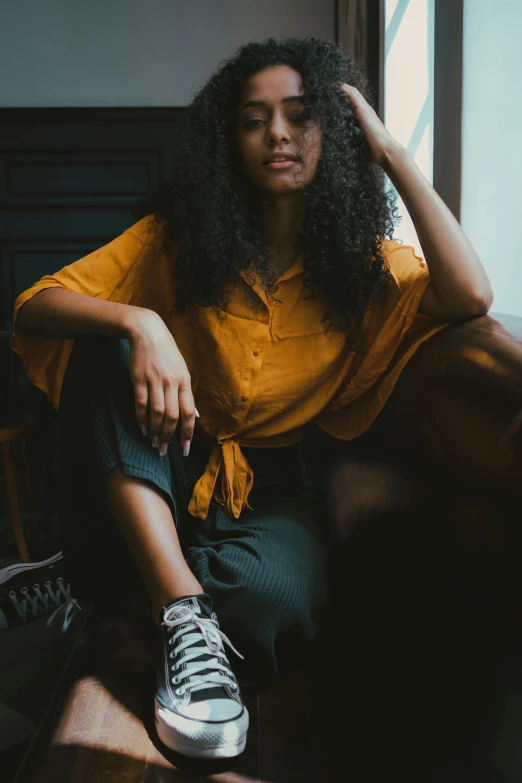 a woman sitting on a couch in front of a window, by irakli nadar, trending on pexels, renaissance, black. yellow, brown shirt, black young woman, curly