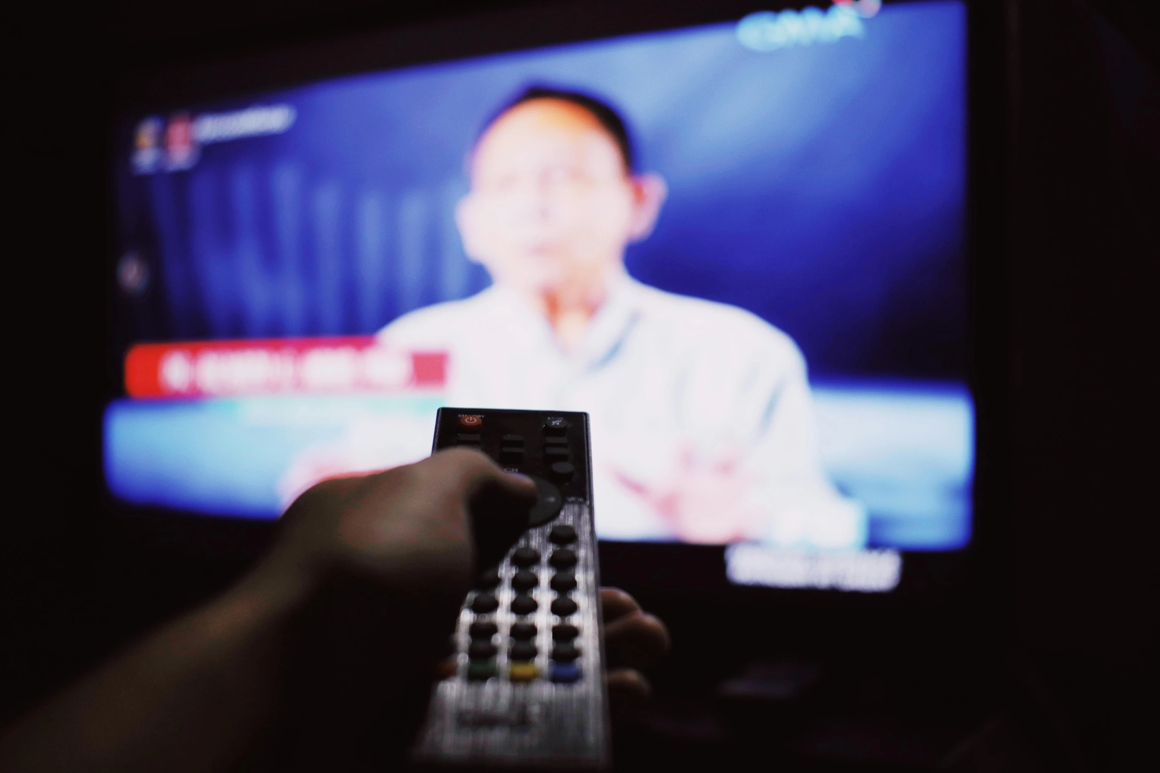 a person holding a remote control in front of a television, pexels, lee kuan yew, view from a news truck, blurred, politics