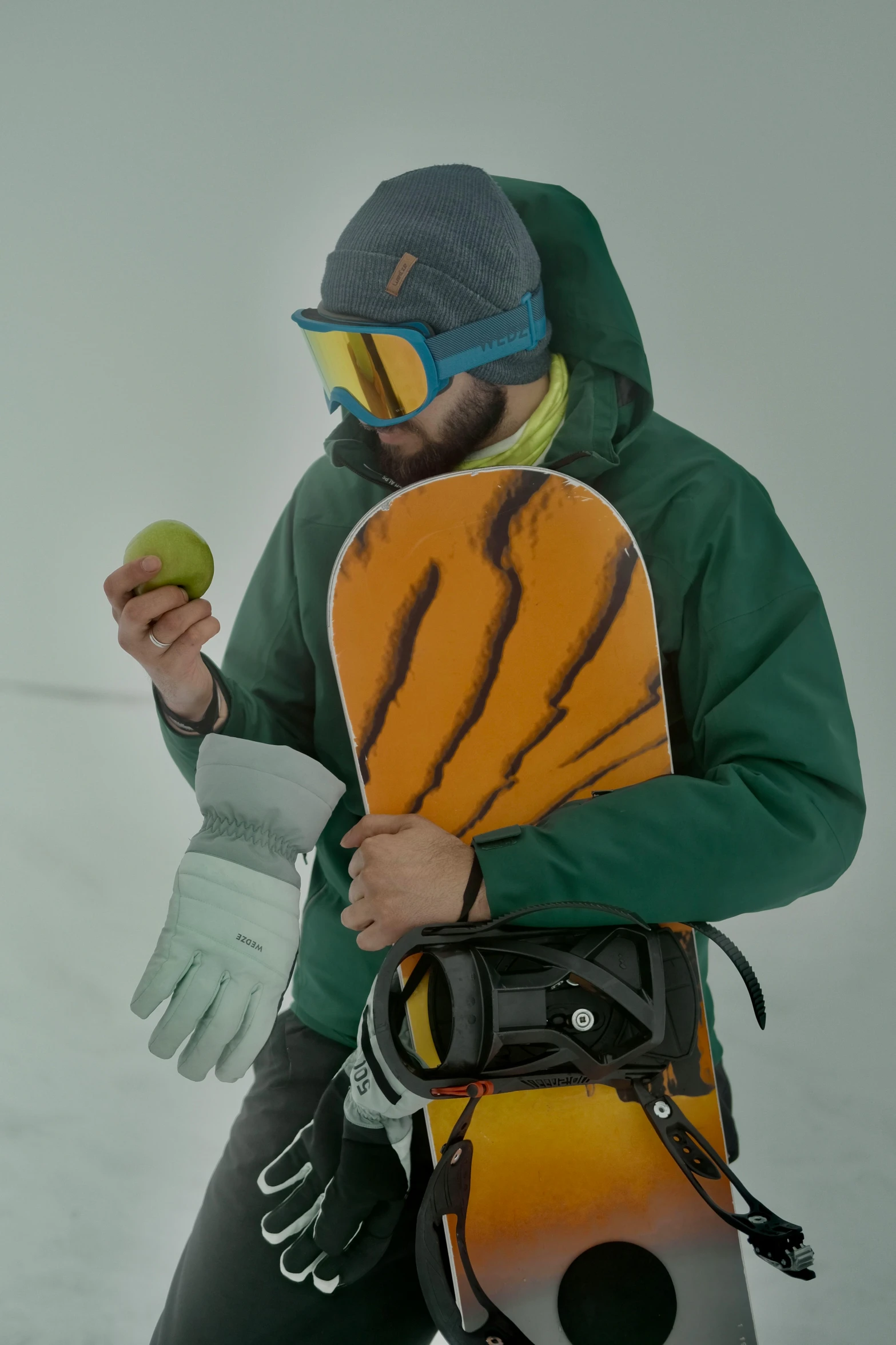 a man holding a snowboard and an apple, orange balaclava, upper body visible, press shot, 2070