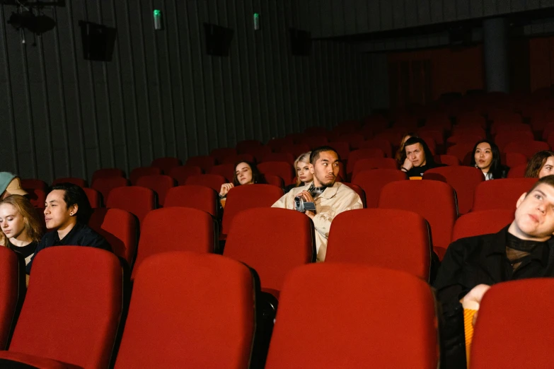 a group of people sitting in rows of red chairs, indie film, ignant, customers, indoor picture