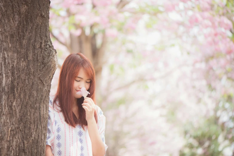 a woman standing next to a tree eating an ice cream cone, by Sengai, pexels contest winner, romanticism, pink flower, avatar image, young asian woman, warm spring
