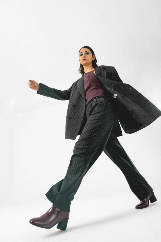 a woman in a suit and boots is walking, an album cover, by Nina Hamnett, unsplash, bauhaus, dynamic dancing pose, baggy pants, non binary model, pinstripe suit