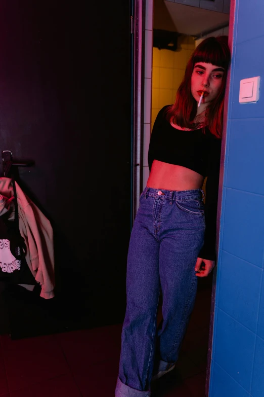 a woman standing in a doorway with a cigarette in her mouth, an album cover, inspired by Elsa Bleda, trending on pexels, happening, jeans pants, locker room, blacklight aesthetic, 90's color photo
