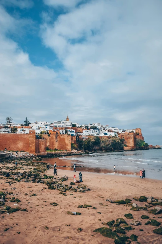 a group of people standing on top of a sandy beach, moorish architecture, villages castles, red sand beach, city walls