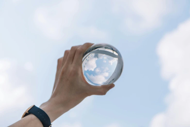 a person holding a glass ball in their hand, inspired by Buckminster Fuller, pexels contest winner, clouds visible, instagram post, magnifying glass, looking upwards