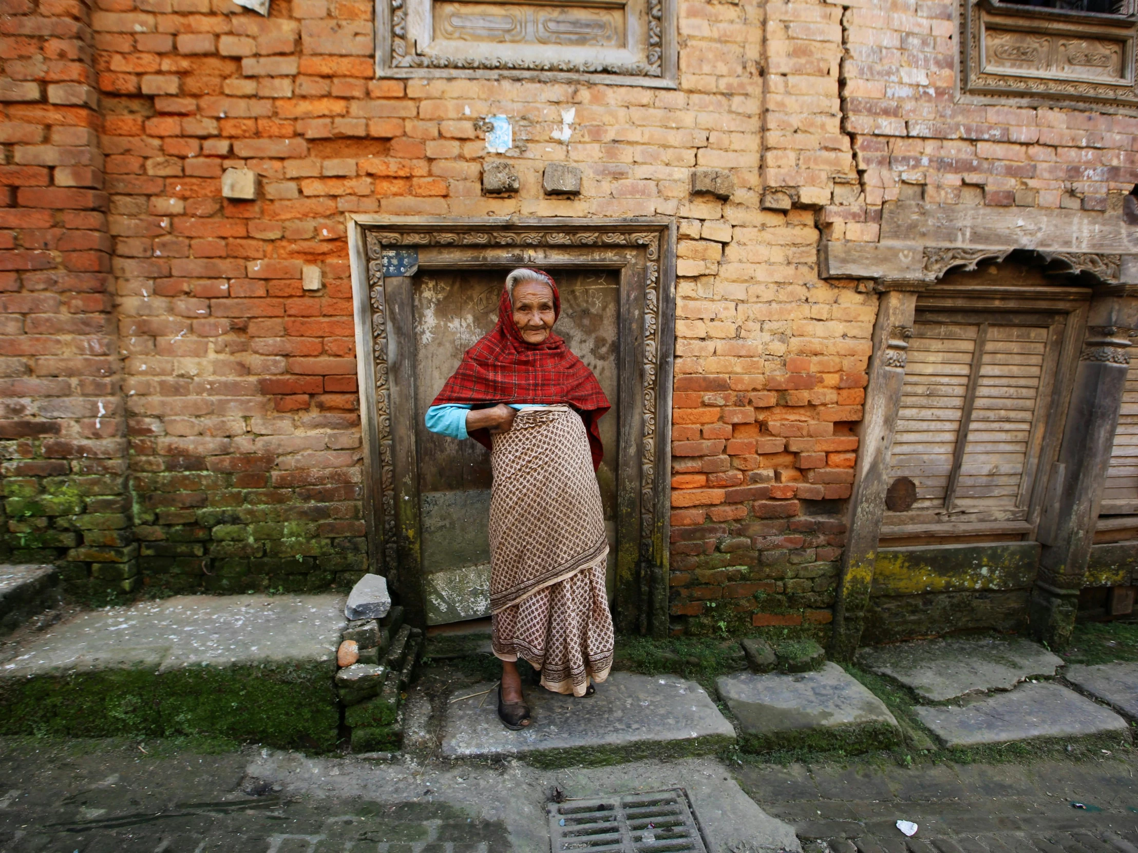 a woman standing in front of a brick building, by Peter Churcher, pexels contest winner, nepal, grandma, dressed in a worn, a cozy