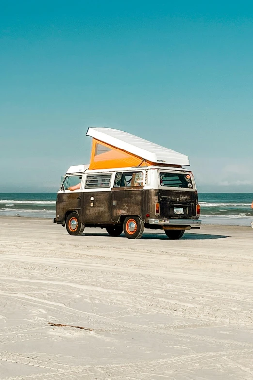 a van sitting on top of a sandy beach next to the ocean, profile image