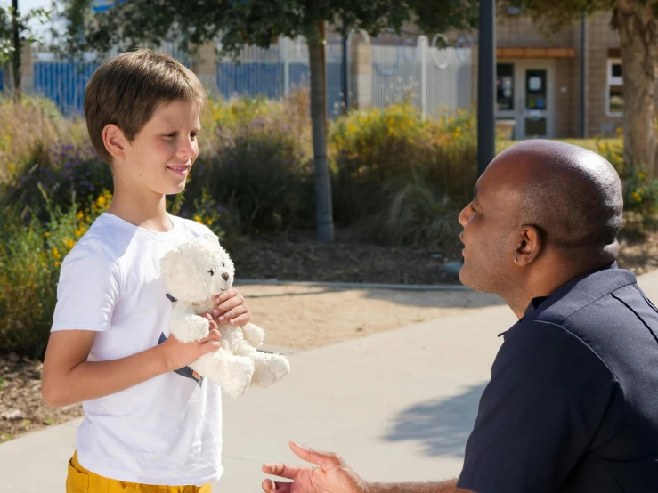 a man standing next to a little boy holding a teddy bear, inspired by William Berra, pexels contest winner, calmly conversing 8k, varying ethnicities, private school, scene from live action movie