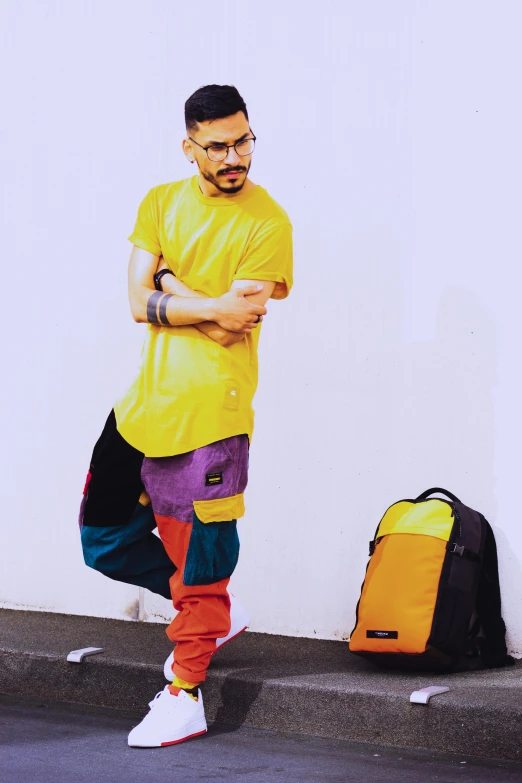 a man in a yellow shirt leaning against a wall, an album cover, instagram, antipodeans, with a backpack, colorful]”, wearing cargo pants, hideki anno