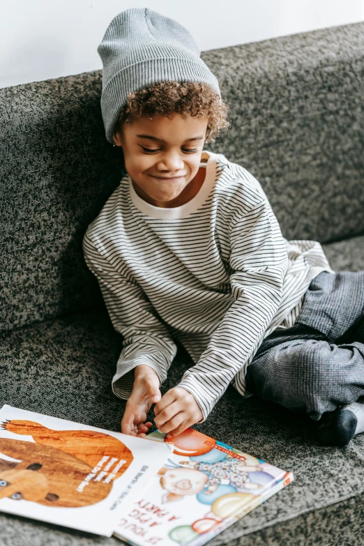 a little boy sitting on a couch reading a book, a child's drawing, pexels contest winner, super cute funky black girl, beanie, gray and orange colours, snacks