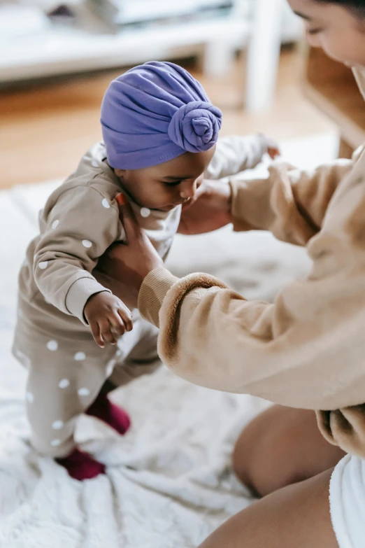 a woman sitting on top of a bed holding a baby, by Arabella Rankin, pexels contest winner, walking to the right, turban, holding each other hands, soft shapes