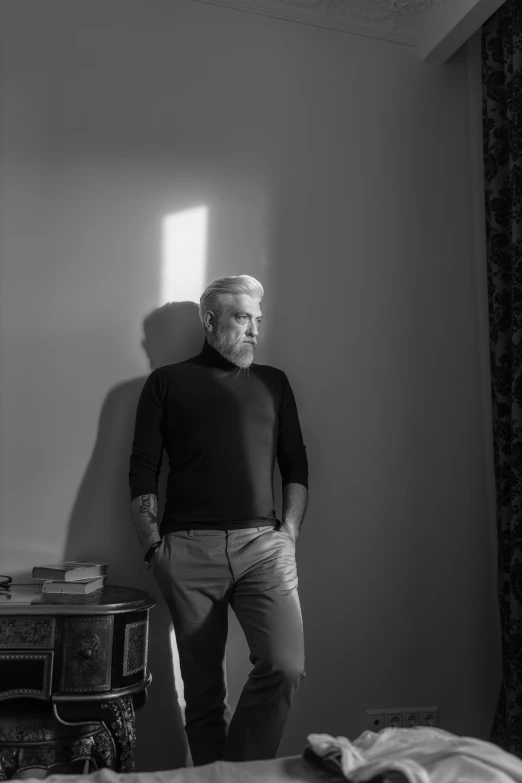 a man standing next to a bed in a room, a black and white photo, inspired by Yousuf Karsh, a silver haired mad, with backlight, pierce brosnan, rutkowski and caravaggio