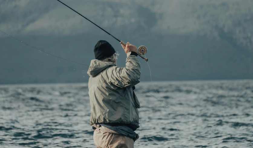 a man that is standing in the water with a fish, fishing pole, skye meaker, flying towards the camera, looking off into the distance