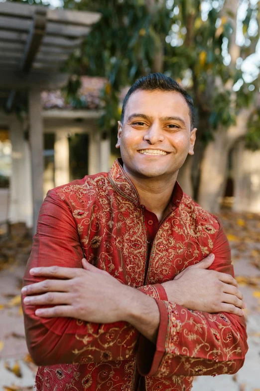 a man in a red jacket posing for a picture, anjali mudra, smiling and looking directly, lgbtq, taken in the late 2010s