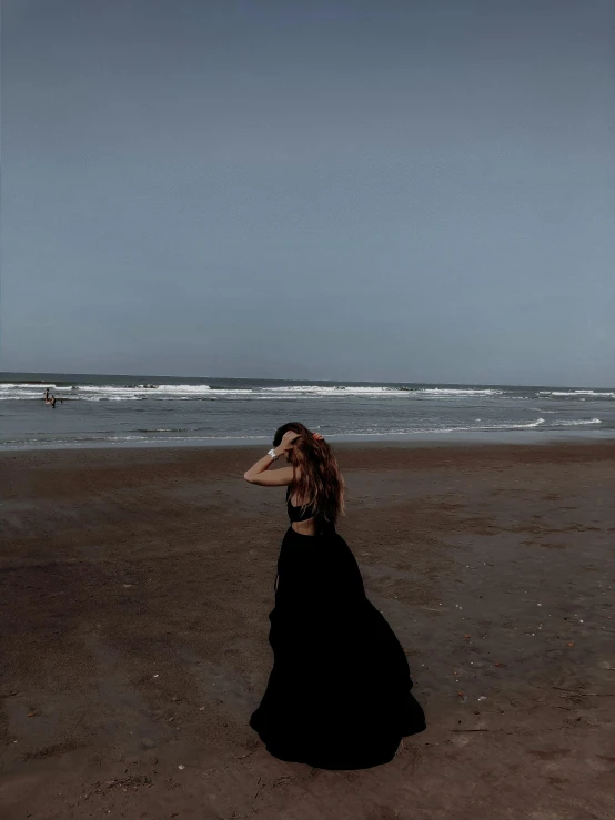 a woman in a black dress standing on a beach, trending on vsco, emaciated black evening gown, ☁🌪🌙👩🏾, sadan vague