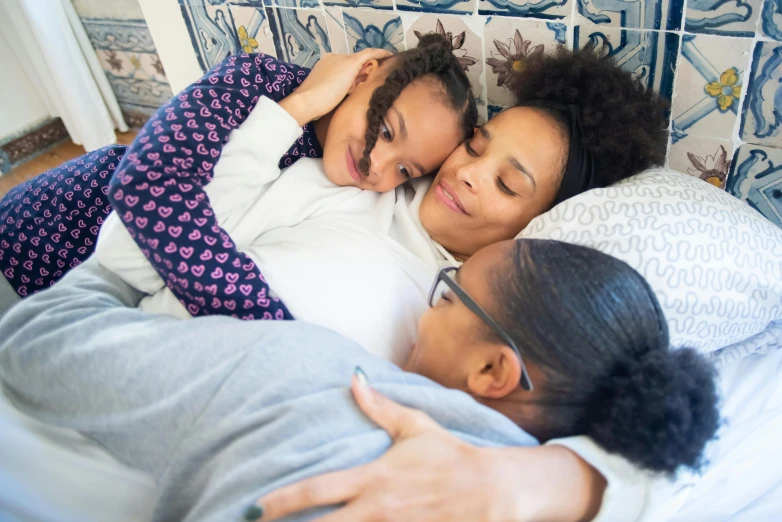 a couple of women laying on top of a bed, by Jessie Algie, pexels contest winner, happening, portrait of family of three, aida muluneh, sweet hugs, medium close up shot