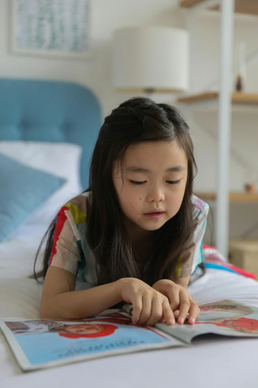 a little girl laying on a bed reading a book, inspired by Li Di, pexels contest winner, process art, asian female, smart looking, a handsome, panels