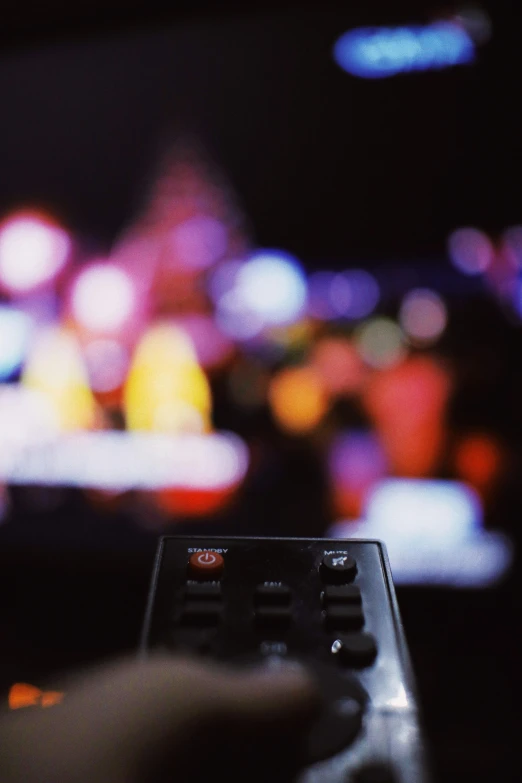 a person holding a remote control in front of a television, inspired by roger deakins, pexels, video art, city lights bokeh, multicoloured, low - angle shot, concert