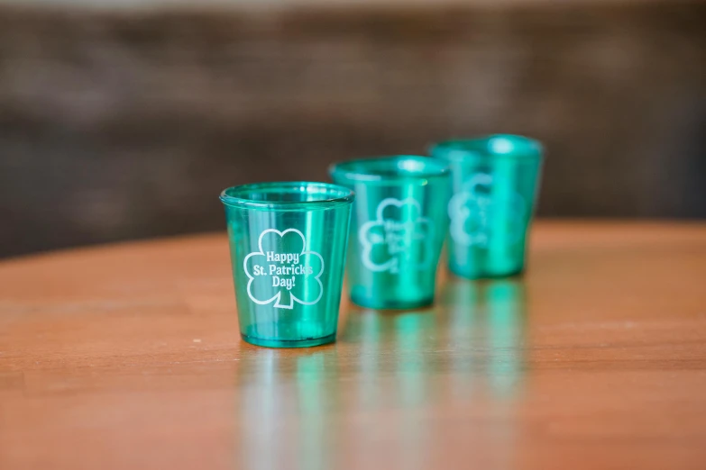 four shot glasses sitting on top of a wooden table, inspired by Don Eddy, clover, teal color graded, happy friend, plastic sheen