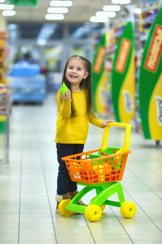 a little girl standing next to a shopping cart, green and yellow, plastic toy, at checkout, feature