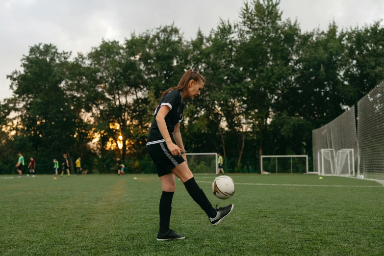 a woman kicking a soccer ball on a field, pexels contest winner, wearing black shorts, 15081959 21121991 01012000 4k, evening time, teenager girl