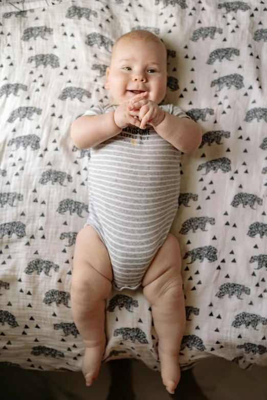 a baby laying on top of a bed next to a pillow, unsplash, happening, hands on hips, patterned, chest legs, grey