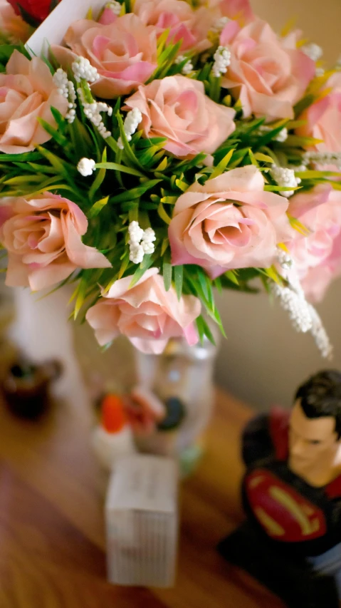 a vase filled with pink flowers on top of a wooden table, flickr, figurines, teenage boy, detail on scene, pastel roses
