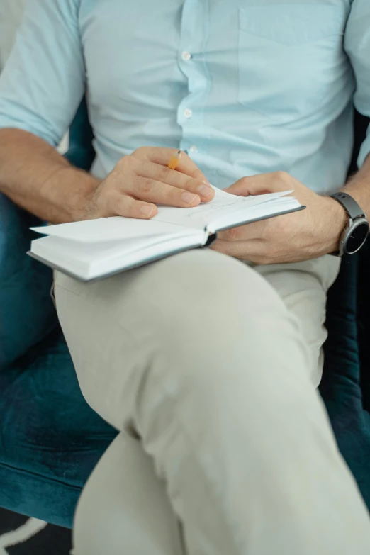 a man sitting on a couch writing in a notebook, comforting, daniel oxford, paul barson, hands crossed