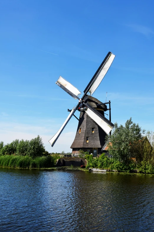 a windmill sitting on top of a body of water, inspired by Willem Hondius, it's very huge, blue sky, quaint, over-shoulder shot