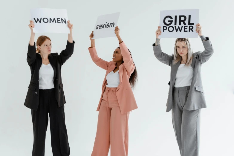 three women holding up signs that say girls power, by Emma Andijewska, trending on pexels, on a pale background, office clothes, on a gray background, standing upright