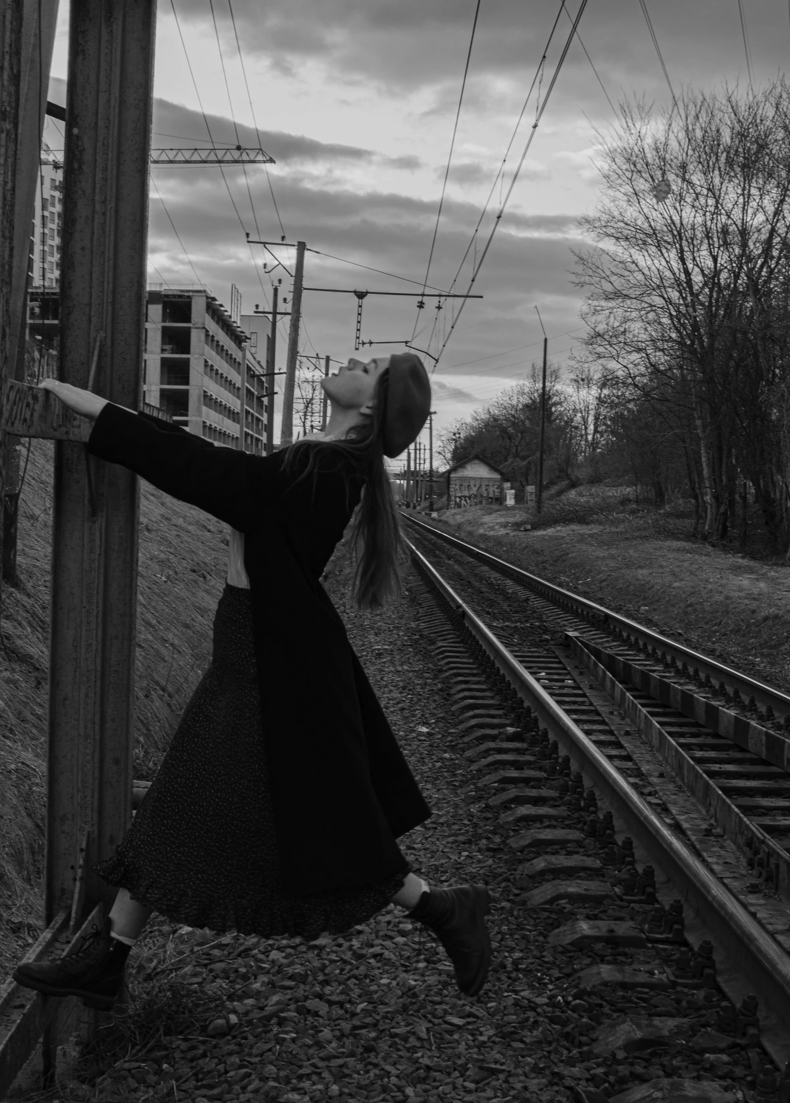 a black and white photo of a woman on a train track, by Lucia Peka, dark ballerina, woman in black robes, standing with her back to us, taken in 2 0 2 0