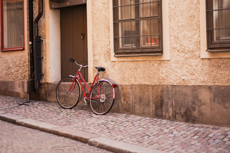 a red bicycle parked in front of a building, by Jesper Knudsen, pexels contest winner, cobblestone, warm coloured, swedish, 🚿🗝📝