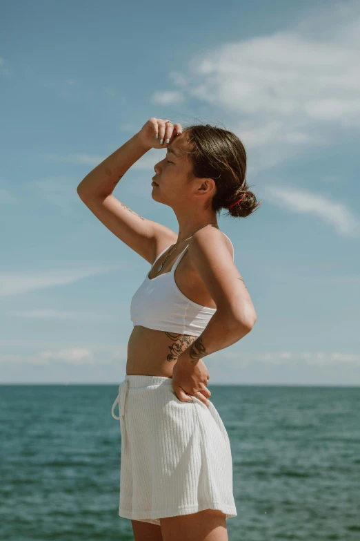 a woman standing on top of a beach next to the ocean, wearing : tanktop, profile image, white outfit, cooling