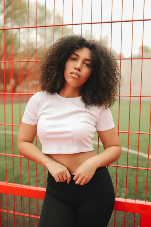 a woman standing in front of a fence, wearing crop top, curly black hair, soccer, 2019 trending photo