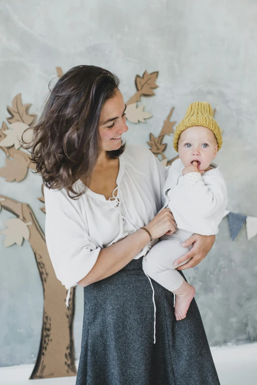 a woman holding a baby in her arms, inspired by Elsa Beskow, pexels contest winner, cardboard cutout, crown made of felt, autumn, white and yellow scheme