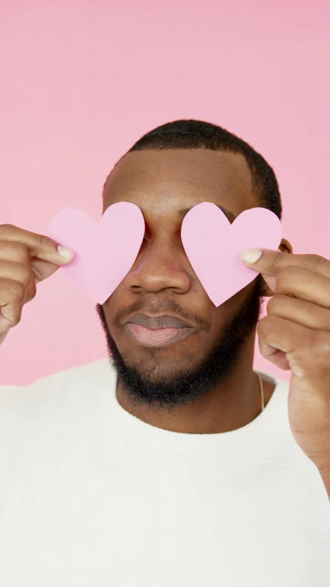 a man holding two pink hearts in front of his eyes, by Dulah Marie Evans, trending on pexels, pride month, jamal campbell, cut out, cutest