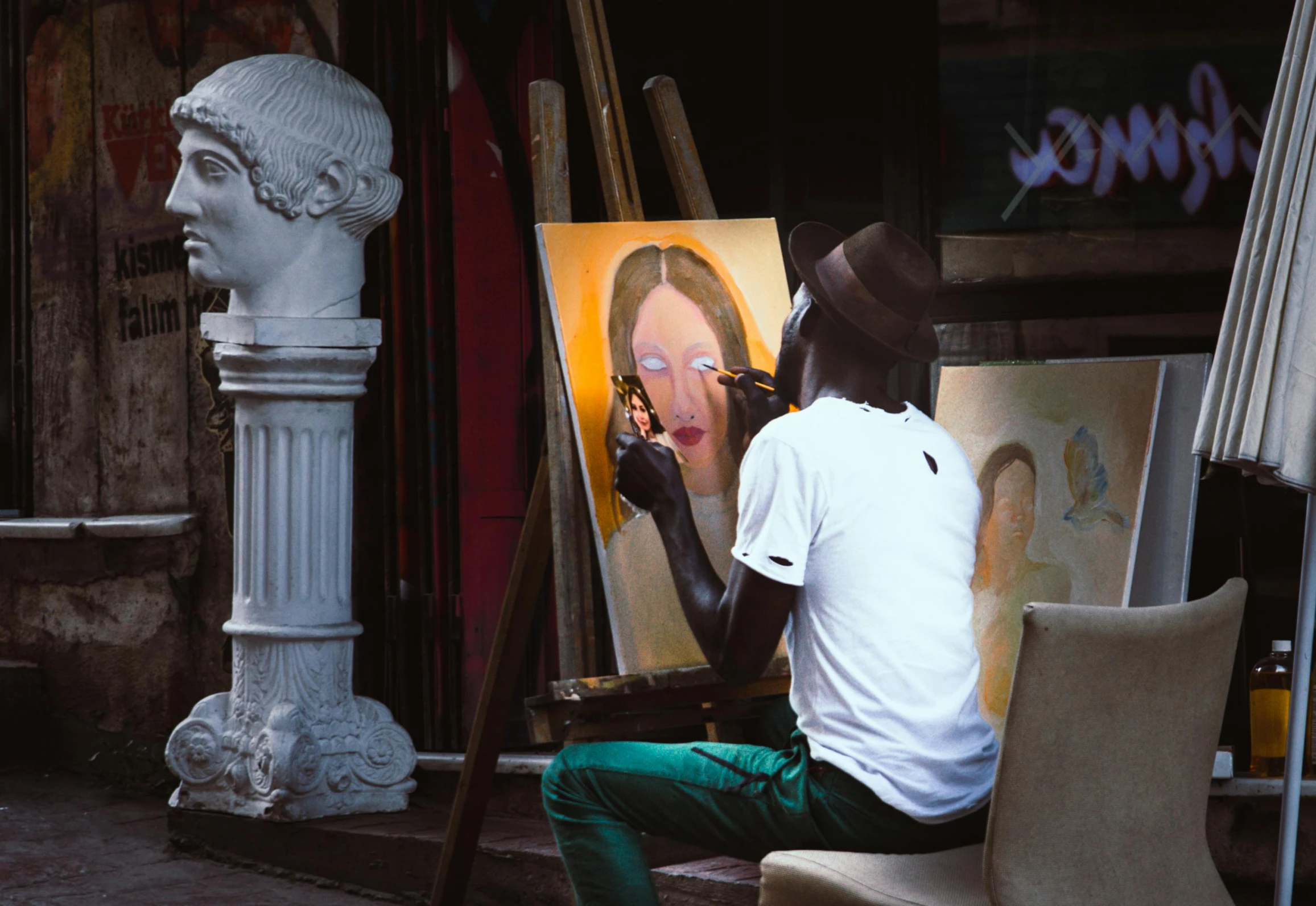 a man that is sitting in front of a painting, by Douglas Shuler, pexels contest winner, figurative art, paint-on-glass painting, street life, stands at a his easel, raphael personnaz