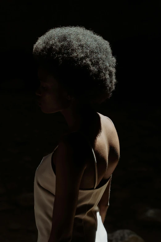 a woman in a white dress standing in the dark, inspired by Carrie Mae Weems, unsplash, natural hair, back - lit, medium format. soft light, ignant